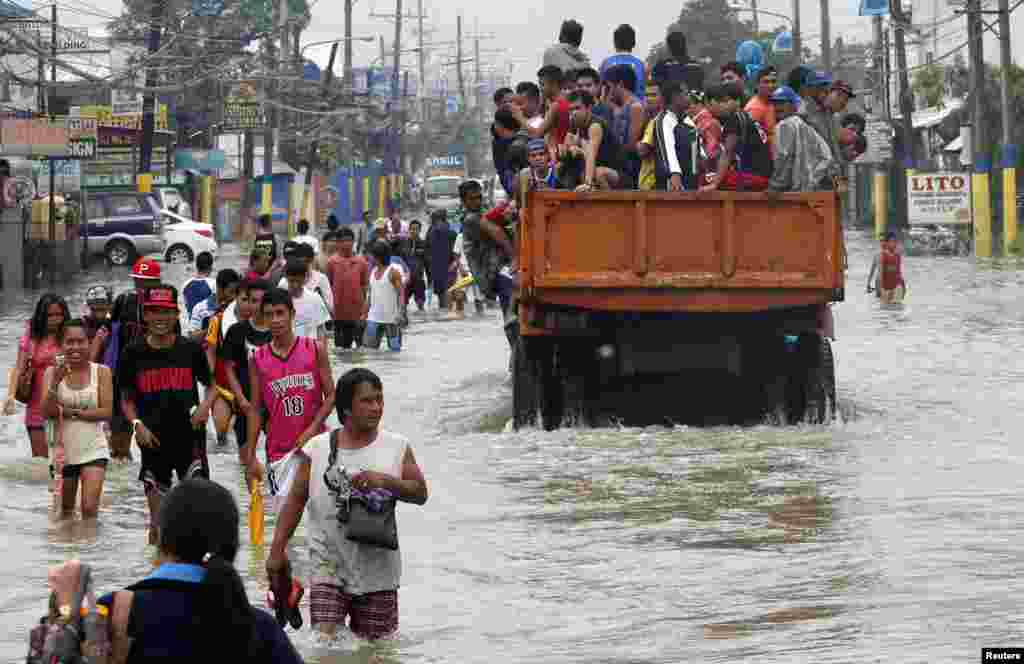 Flood victims are evacuated on a truck while other residents wade through floodwaters on a street in Bacoor near Manila, August 20, 2013.