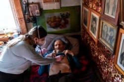 Dr. Viktoria Mahnych, wearing face mask against coronavirus, checks on a COVID-19 patient with a stethoscope at at his home in Iltsi village, Ivano-Frankivsk region of Western Ukraine, Wednesday, Jan. 6, 2021