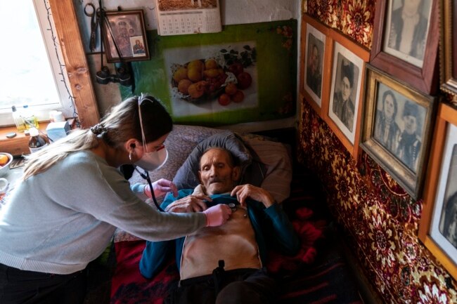 Dr. Viktoria Mahnych, wearing face mask against coronavirus, checks on a COVID-19 patient with a stethoscope at at his home in Iltsi village, Ivano-Frankivsk region of Western Ukraine, Wednesday, Jan. 6, 2021