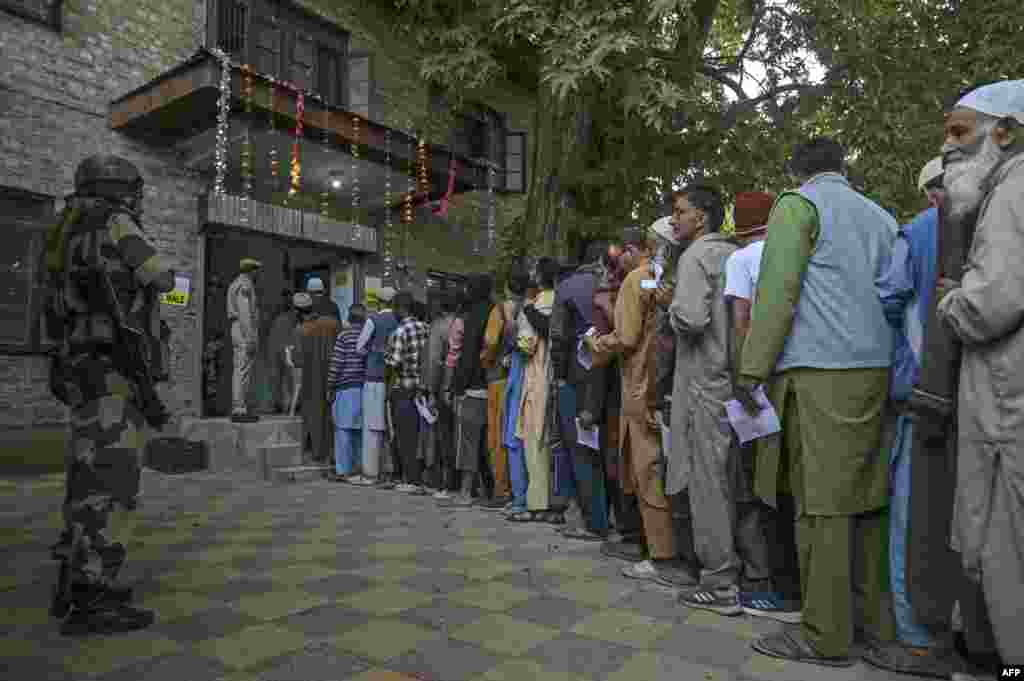 An Indian security personnel stands guard as voters queue up to cast their ballots at a polling station during the first phase of assembly elections in Pulwama, south of Srinagar.