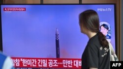 A woman walks past a television screen showing a news broadcast with file footage of a North Korean missile test, at a railway station in Seoul on July 12, 2023.