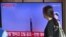 A woman walks past a television screen showing a news broadcast with file footage of a North Korean missile test, at a railway station in Seoul on July 12, 2023.