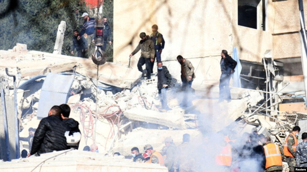 People inspect the damage at the site of a strike in the Mazzeh neighborhood of Damascus