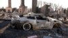 A sign sits on the ground next to a car destroyed by the Palisades Fire, in the Pacific Palisades neighborhood in Los Angeles, California, Jan. 14, 2025.