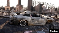 A sign sits on the ground next to a car destroyed by the Palisades Fire, in the Pacific Palisades neighborhood in Los Angeles, California, Jan. 14, 2025.