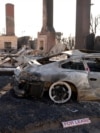 A sign sits on the ground next to a car destroyed by the Palisades Fire, in the Pacific Palisades neighborhood in Los Angeles, Jan. 14, 2025.