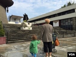 A grandmother and granddaughter look up at a statue of Pope John Paul II at the Ark of the Lord church in Krakow, Apr. 23, 2014. (Jerome Socolovsky/VOA)