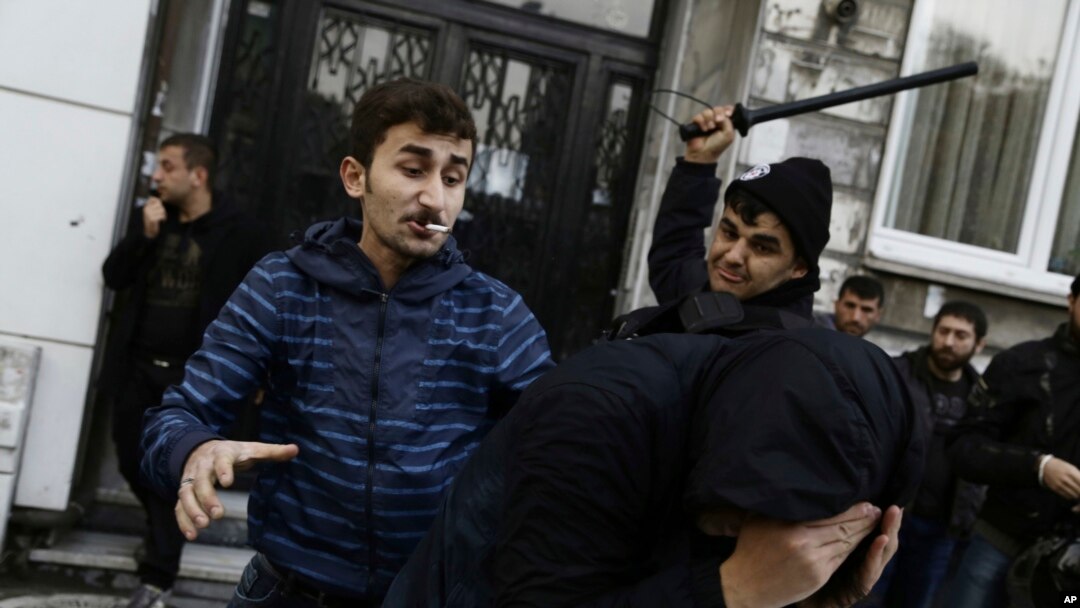 A civilian, left, and a security officer beat a protester as riot police use water cannons to disperse people protesting the detentions of 12 lawmakers from pro-Kurdish Peoples' Democratic Party, or HDP, in Istanbul, Nov. 5, 2016.