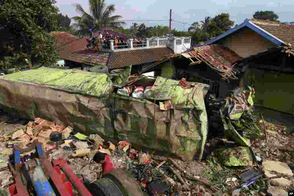 Warga memeriksa bangkai truk kontainer yang menabrak beberapa rumah di Cianur, Jawa Barat, Indonesia. Polisi mengatakan pengemudi truk sepertinya kehilangan kontrol ketika rem kendaraannya blong, dan menabrak angkot serta puluhan sepeda motor dan sebuah pabrik sebelum menyeberang jalan, menimpa sejumlah mobil dan menghantam beberapa rumah.