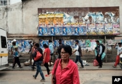 Pedestrians pass a wall with election posters in Antananarivo, Madagascar, Nov. 6, 2018 on the eve of elections in the Indian Island nation.