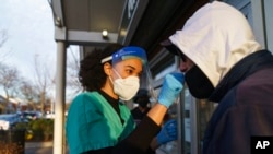 Maya Goode, a COVID-19 technician, left, performs a COVID-19 test on Mark Serra outside Asthenis Pharmacy in Providence, R.I., Dec. 7, 2021.