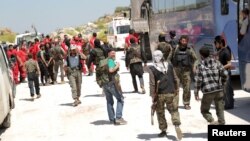 Fighters from a coalition of rebel groups called "Army of Fatah" and members of the Syrian Arab Red Crescent stand near buses and ambulances on the outskirts of Idlib city, preparing to enter the two besieged Shi'ite towns of al-Foua and Kefraya to evacu