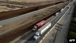 Trucks queue near the border wall before crossing to the U.S. at Otay commercial port in Tijuana, Baja California state, Mexico, Jan. 22, 2025. Starting Saturday, President Donald Trump will place 25% tariffs on imports from Canada and Mexico and 10% tariffs on goods from China.