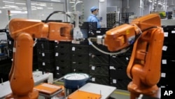 A Chinese worker is seen behind orange robot arms at Rapoo Technology factory in the southern Chinese industrial boomtown of Shenzhen, Aug. 21, 2015. Automation could wipe out two thirds of jobs in some countries, the World Bank warns.