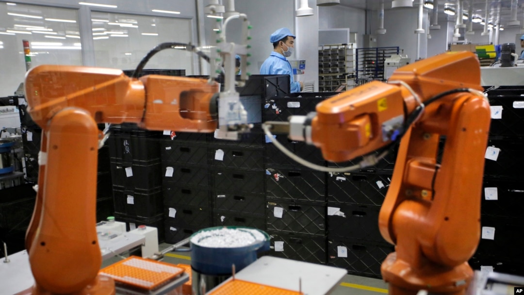 Seorang pekerja di China tampak di belakang lengan robot berwarna oranye di pabrik Rapoo Technology di kota Shenzhen, China, 21 Agustus 2015 (foto: AP Photo/Vincent Yu)