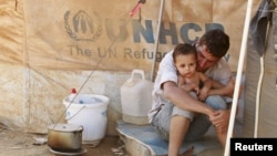 A Syrian refugee holds his child as he sits by his tent at Al Zaatri refugee camp in the Jordanian city of Mafraq, near the border with Syria, September 9, 2012. 