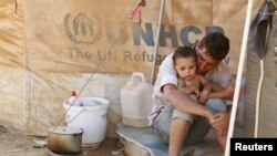 A Syrian refugee holds his child as he sits by his tent at Al Zaatri refugee camp in the Jordanian city of Mafraq, near the border with Syria, Sept. 9, 2012. 