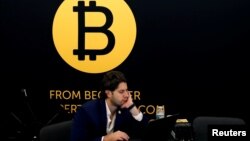 FILE - A man works on a laptop beneath the Bitcoin logo at the Consensus 2018 blockchain technology conference in New York City, May 16, 2018. 