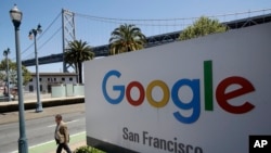 FILE - A man walks past a Google sign outside with a span of the Bay Bridge at rear in San Francisco, May 1, 2019.