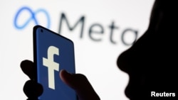FILE - A woman holds a smartphone with the Facebook logo in front of a display of Facebook's new rebrand logo Meta in this illustration picture taken Oct. 28, 2021.