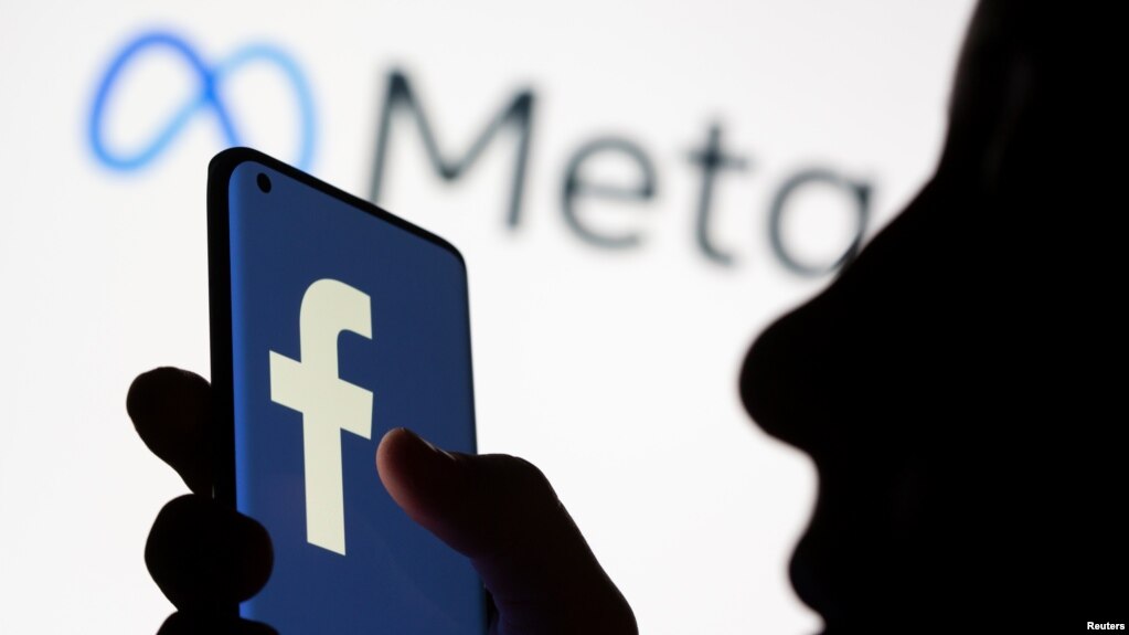 FILE - A woman holds a smartphone with the Facebook logo in front of a display of Facebook's new rebrand logo Meta in this illustration picture taken October 28, 2021.