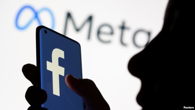 FILE - A woman holds a smartphone with the Facebook logo in front of a display of Facebook's new rebrand logo Meta in this illustration picture taken October 28, 2021.