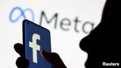 A woman holds a smartphone with the Facebook logo in front of a display of Facebook's new rebrand logo Meta in this illustration picture taken Oct. 28, 2021.