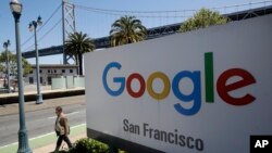 A man walks past a Google sign outside with a span of the Bay Bridge at rear in San Francisco, May 1, 2019.