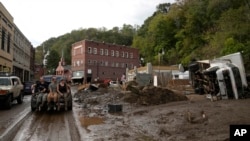 People ride in the back of a pickup truck on a mud-covered street left in the aftermath of Hurricane Helene, in Marshall, North Carolina, Oct. 1, 2024.