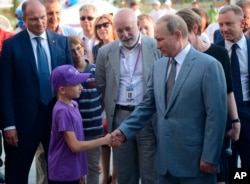 FILE - Russian President Vladimir Putin, right, shakes hands with a boy as he visits the Sirius college for gifted children in the Black Sea resort of Sochi, Russia, Sept. 1, 2015. In center is Russian Renova's CEO Viktor Vekselberg.