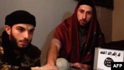 An image grab taken from a video released July 27, 2016, by Amaq News Agency, an online service affiliated with the Islamic State (IS) group, purportedly shows the two men who stormed into a church in the northern French town of Saint-Etienne-du-Rouvray and cut the throat of a 86-year-old priest at the altar, identifying themselves as Abu Jaleel al-Hanafi (L) and Ibn Omar (R) sitting next to the logo of the IS group while pledging allegiance to IS leader Abu Bakr al-Baghdadi. 