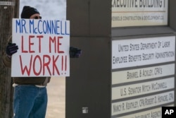 El empleado de la EPA Jeff Herrema, con licencia obligada por el cierre del gobierno, sostiene un cartel en el que pide al líder de la mayoría del Senado, Mitch McConnell "Déjeme trabajar!!", afuera de la oficina de McConnell en Park Hills, Kentucky, el 22 de enero de 2019.
