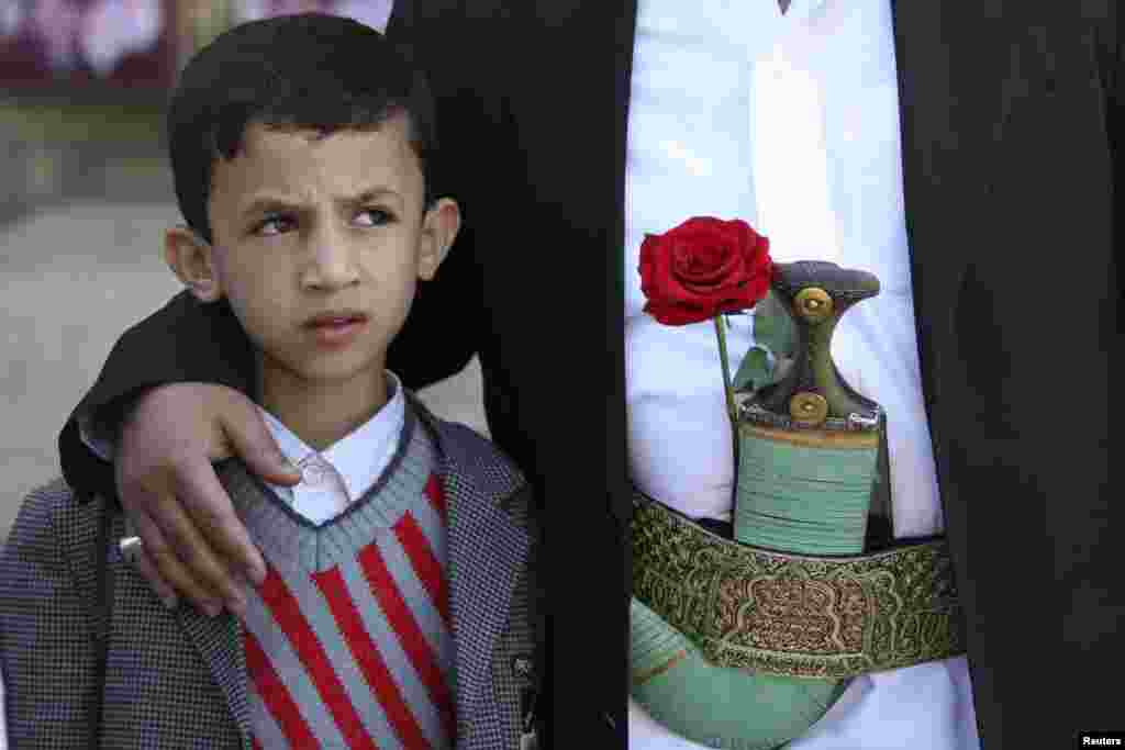 A boy looks on while standing with his father, who a rose placed on his belt, they shop for gifts on Valentine&#39;s Day in Sana&#39;a, Yemen.