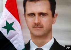 FILE - A man holds a Syrian national flag and a picture of Syrian President Bashar al-Assad during a protest outside the Syrian embassy in Belgrade, Serbia, April 15, 2018.