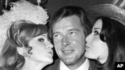 Roger Moore reçoit un baiser de Miss Grande Bretagne et de Miss USA à Londres, le 4 novembre 1971.