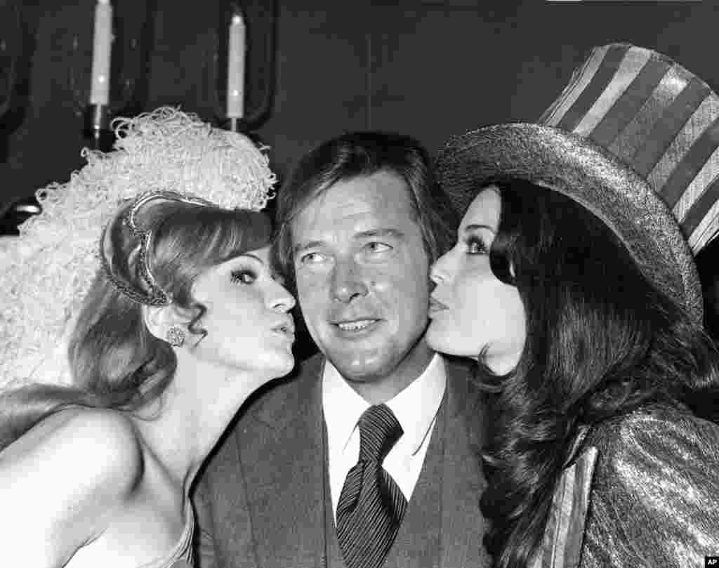 影星罗杰&middot;摩尔1971年在世界小姐选美的午餐会上接受英国小姐和美国小姐的亲吻。 罗杰&middot;摩尔的家人2017年5月23日说，他在和癌症短期搏斗后去世。 &nbsp;