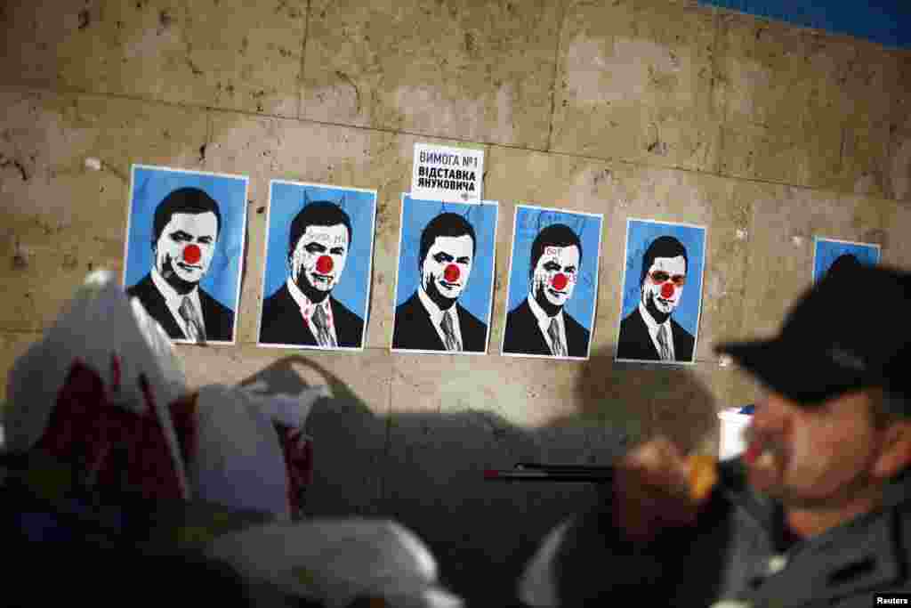 A man eats next to defaced posters depicting Ukrainian Viktor Yanukovych at Independence Square, Kyiv, Dec. 4, 2013.