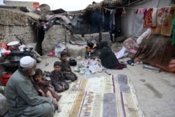 In this Oct. 29, 2019 photo, Yousuf, who fled with his family from his home in eastern Afghanistan eight years ago to escape the war, sits with children while his wife burns plastic as she makes tea, in Kabul, Afghanistan. (AP Photo/Rahmat Gul)