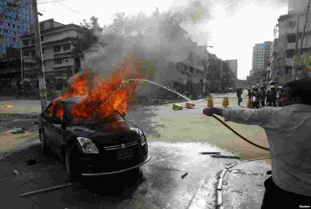 A man sprays water on a car set on fire by activists of the Jemaat-e-Islami party protesting the revised sentencing of Abdul Quader Mollah, Dhaka, Sept. 17, 2013.