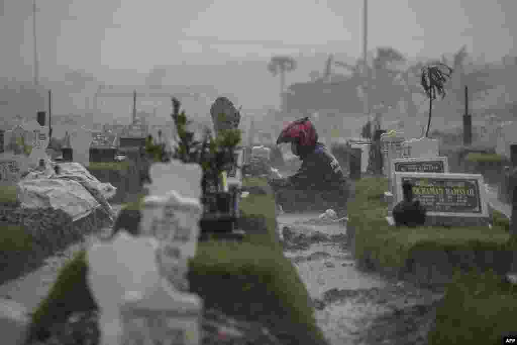 A man sits by the grave of a COVID-19 victim during rainy weather at Keputih cemetery in Surabaya, Indonesia.