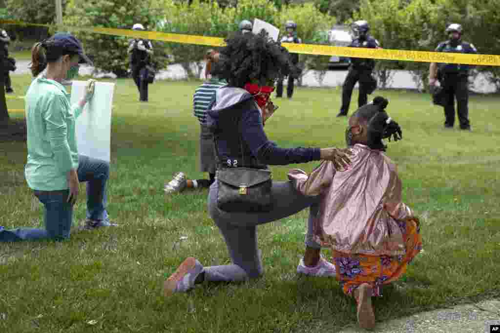 Ericka Ward-Audena, of Washington, puts her hand on her daughter Elle Ward-Audena, 7, as they take a knee in front of a police line during a protest of President Donald Trump's visit to the Saint John Paul II National Shrine, Tuesday, June 2, 2020, in Washington. "I wanted my daughter to see the protests, Ward-Audena said. (AP Photo/Jacquelyn Martin)