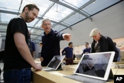 Apple CEO Tim Cook points out the new 9.7 inch iPad Pro to a customer during a visit to the Apple Store, in Palo Alto, California, March 31, 2016..