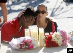 Pamela Tilton, right, comforts Che James-Riley, 18, as they light a candle at a memorial for the victims of the shooting at Marjory Stoneman Douglas High School, Feb. 15, 2018, in Parkland, Florida.