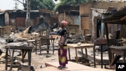 A woman stands in front of burnt buildings in Kachia village, where violence erupted last week, in Nigeria's northern state of Kaduna, April 28, 2011