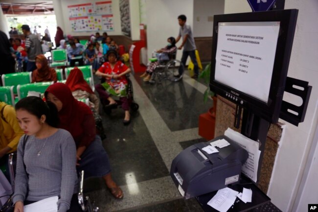 FILE - Patients wait near a queue number dispenser affected by WannaCry attack at Dharmais Cancer Hospital in Jakarta, Indonesia, May 15, 2017.