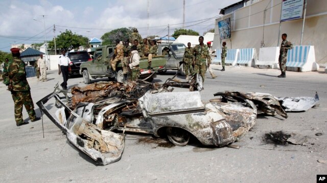 FILE - Somali soldiers stand near the wreckage of car bomb that was detonated at the main gate of the presidential palace in Mogadishu, July, 9, 2014.