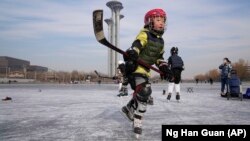 A child plays ice hockey near the Beijing Olympics Tower in Beijing, China January 18, 2022. (AP Photo/Ng Han Guan)