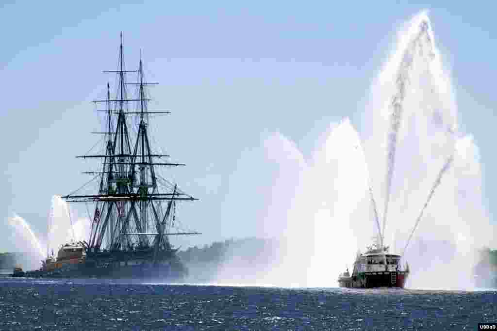 Kapal induk USS Constitution dikawal oleh kapal penyelamat kebakaran Massport di kota Boston, Massachusetts.