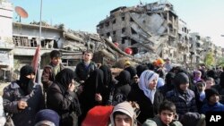 FILE - Hundreds of Syrians mingle amid rubble before going out of town to buy food and other essential materials as they wait in line at a military checkpoint in the town of Beit Sahm, south of the capital, Damascus, Syria, Jan. 14, 2015.