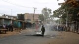 A Kenyan police officer tries to put out flames from a burning tire in Nairobi’s Kibera slum, Aug. 12, 2017. (J. Craig/VOA)